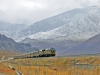 Hochgebirge: Zug der Lhasabahn auf einem Bahndamm vor der eindrucksvollen Hochgebirgskulisse.